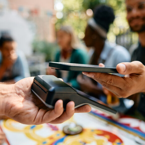 Close up of man using smart phone while paying to a waiter in a cafe.